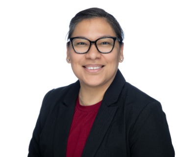 Picture of woman in glasses smiling for headshot. She is wearing a red shirt and a black coat. 